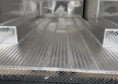 Empty aluminum cargo bed with diamond-plate walls and ribbed floor, inside a utility truck/trailer.