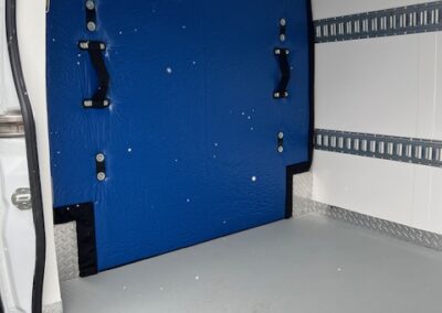 Interior of a white cargo van showing a blue insulated wall panel and metal cargo rails along the side walls, empty floor.