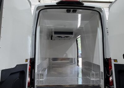 Open rear of a white cargo van with a diamond-plate metal floor and insulated interior, viewed from outside with doors wide open.