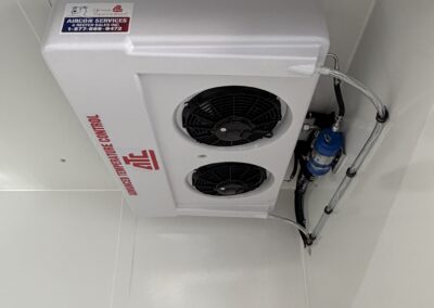 Ceiling-mounted white HVAC unit with two round fans and labeled safety stickers, including '404A Moving Parts' and a blue refrigerant canister nearby.